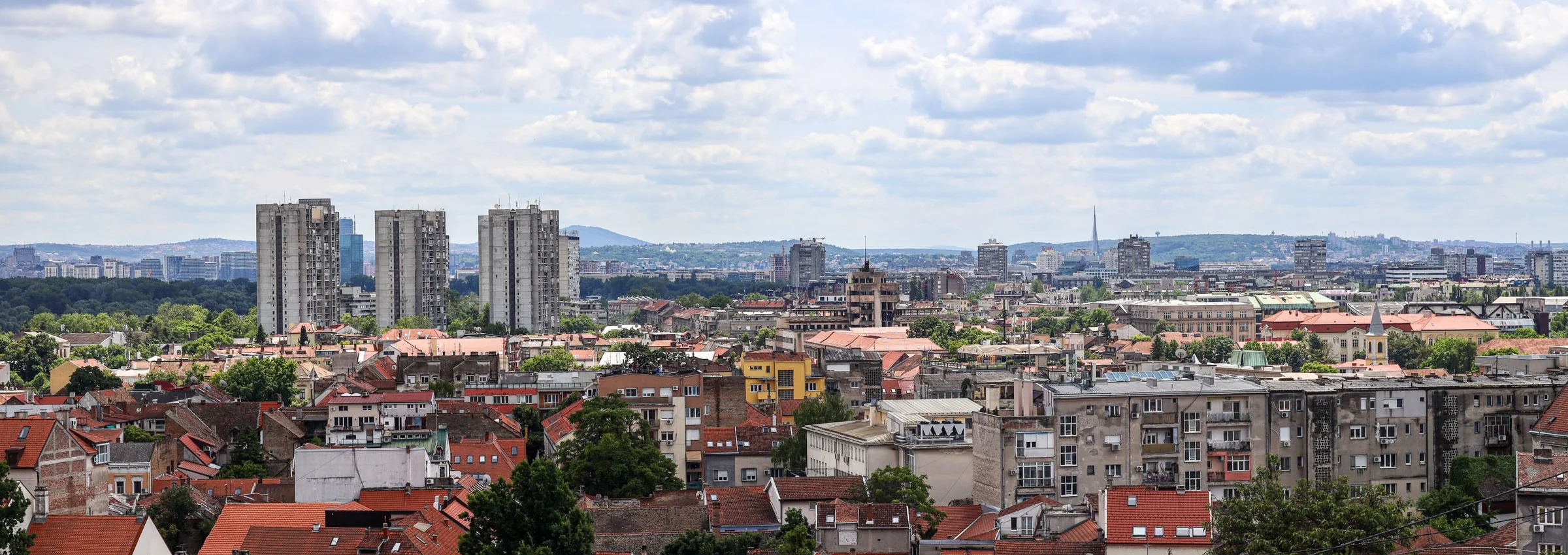 A panoramic view of Belgrade with red rooftops, green trees and a blue sky